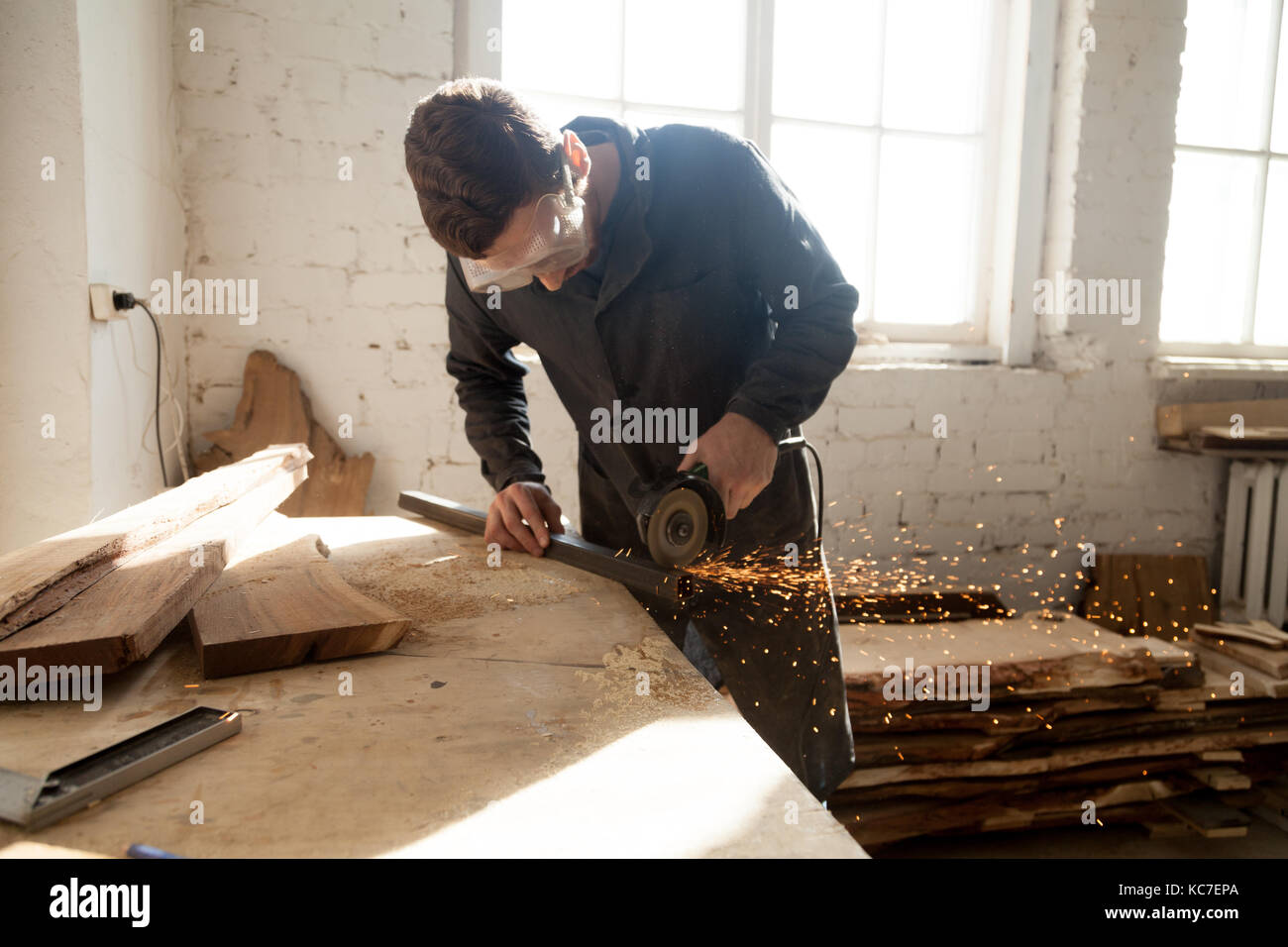 Handwerker in Schutzbrille Schneiden von Stahl plank auf der Workbench mit Winkelschleifer in Werkstatt. Schreiner mit der Arbeit an einem neuen Projekt starten Eigene Stockfoto