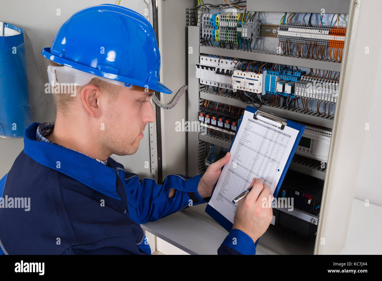 Junge männliche Techniker Holding Zwischenablage während der Prüfung Sicherungskasten Stockfoto