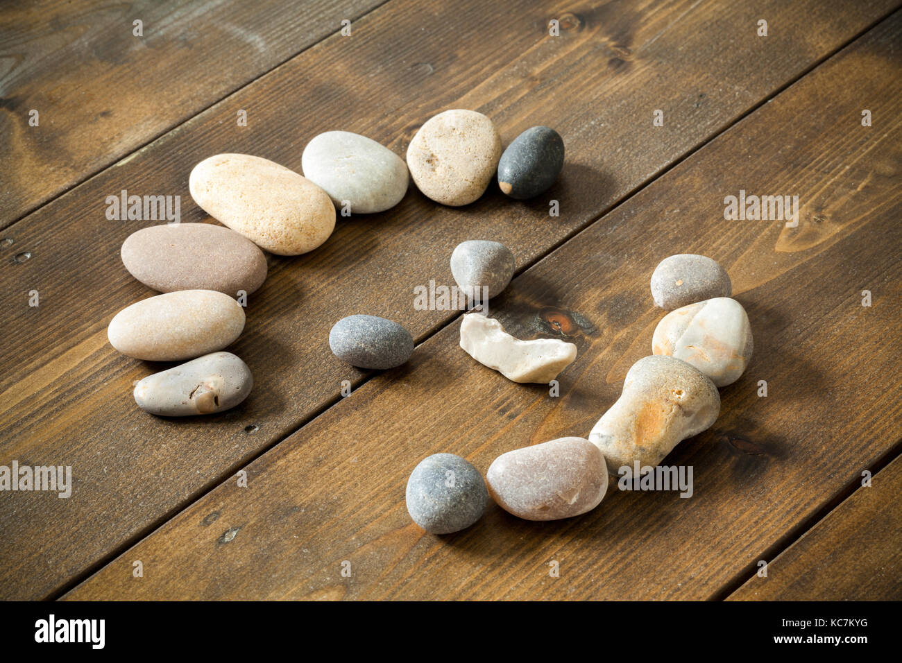 Glücklich lächelnde Gesicht von Beach Pebbles auf einer hölzernen rustikalen Tisch. Konzepte für Gesundheit, Glück, Heilung, Stockfoto