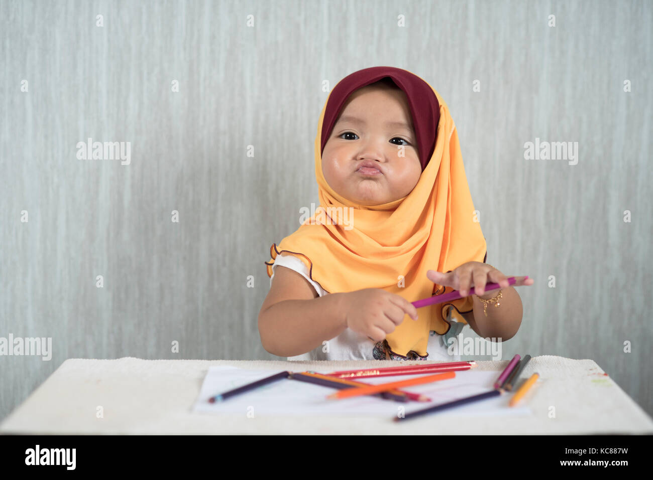 Asiatische Kleinkind/Baby girl Hijab tragen ist Spaß lernen Bleistifte zu verwenden, während Sie lustiges Gesicht. Bildung Konzept. smiling Baby/Kleinkind Stockfoto