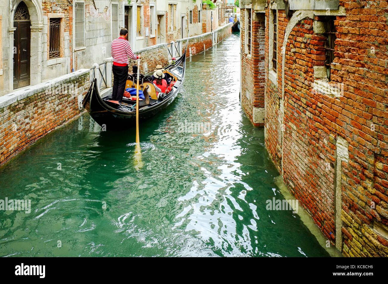 Ein gondoliere nimmt eine Gruppe von Touristen auf einem schmalen Kanal in Venedig, Italien Stockfoto