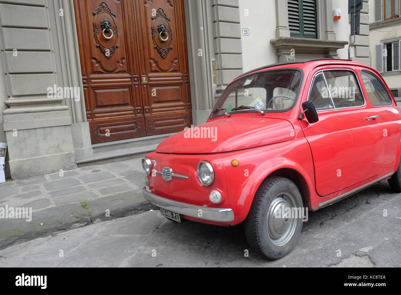 Rot Fiat 500 auf der Straße vor einem alten braun Holz Eingang geparkt. Classic vintage Modell. Florenz, Italien Stockfoto