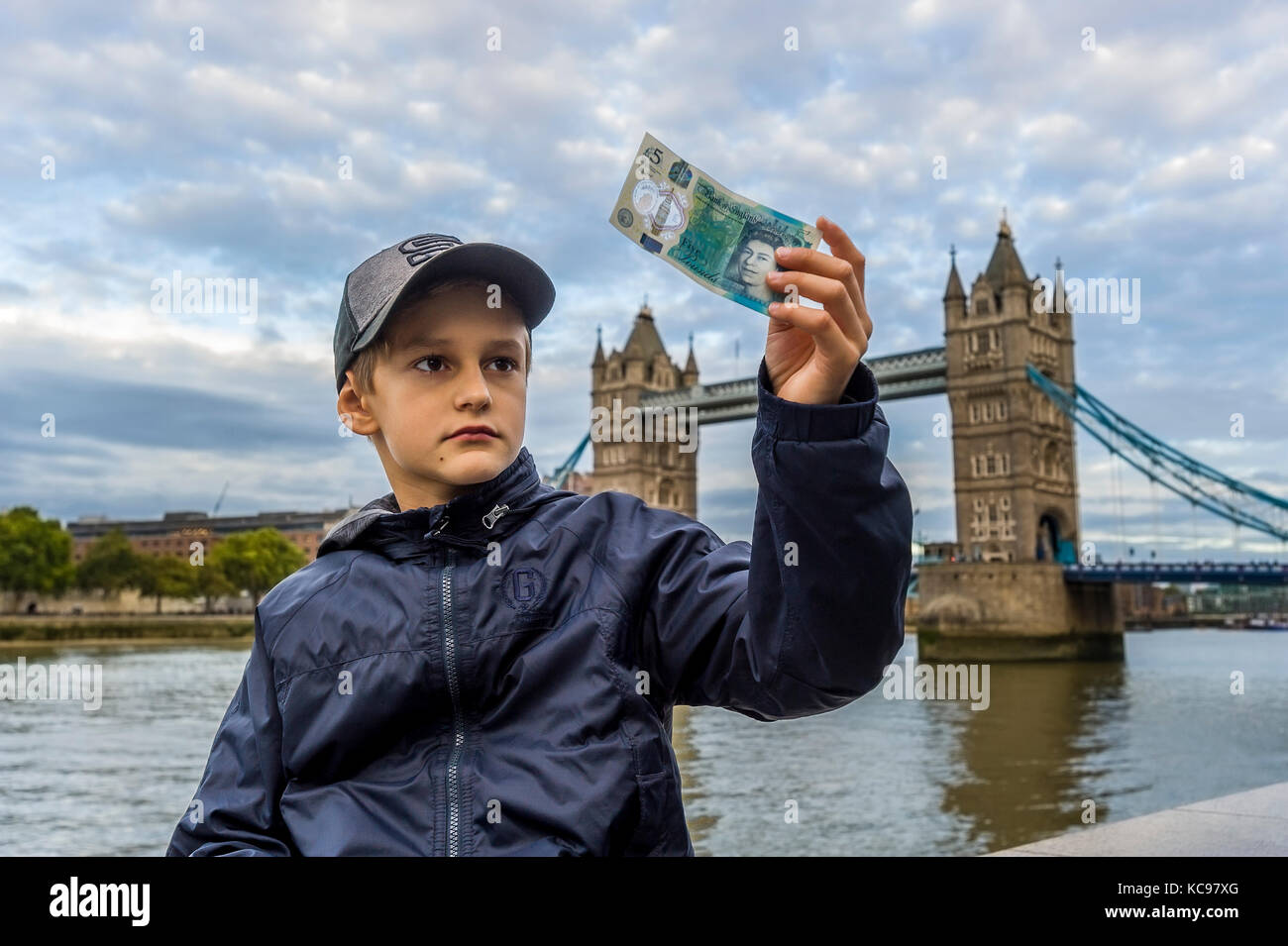 Junge in Baseball Cap halten und auf der Suche nach neuen britischen 5 Pfund Banknote Stockfoto