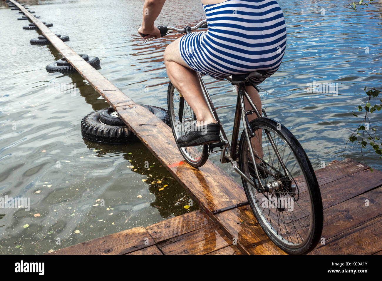 Tschechisches Festival, Ein Radfahrer auf einer hölzernen Fußbrücke versucht, den Teich zu überqueren, ein ungewöhnliches Sportrad über das Wasser, ein Fahrradanzug gestreift Stockfoto