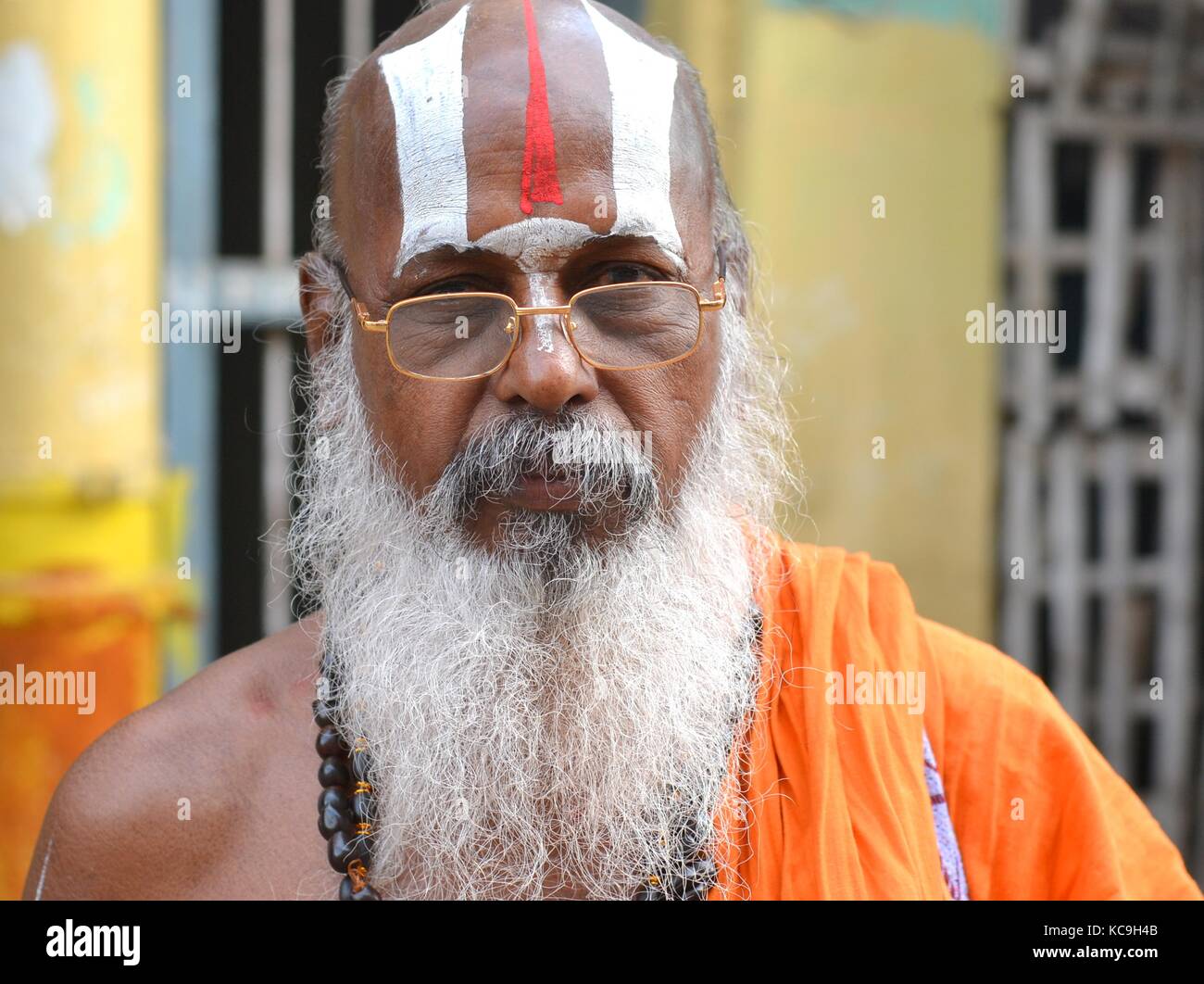Der alte Vaishnavite Brahmin (hinduistischer Priester, der Vishnu anbetet) mit langem weißem Bart und kunstvollem Urdhva-Pundra auf der Stirn in einem orangefarbenen Bademantel Stockfoto