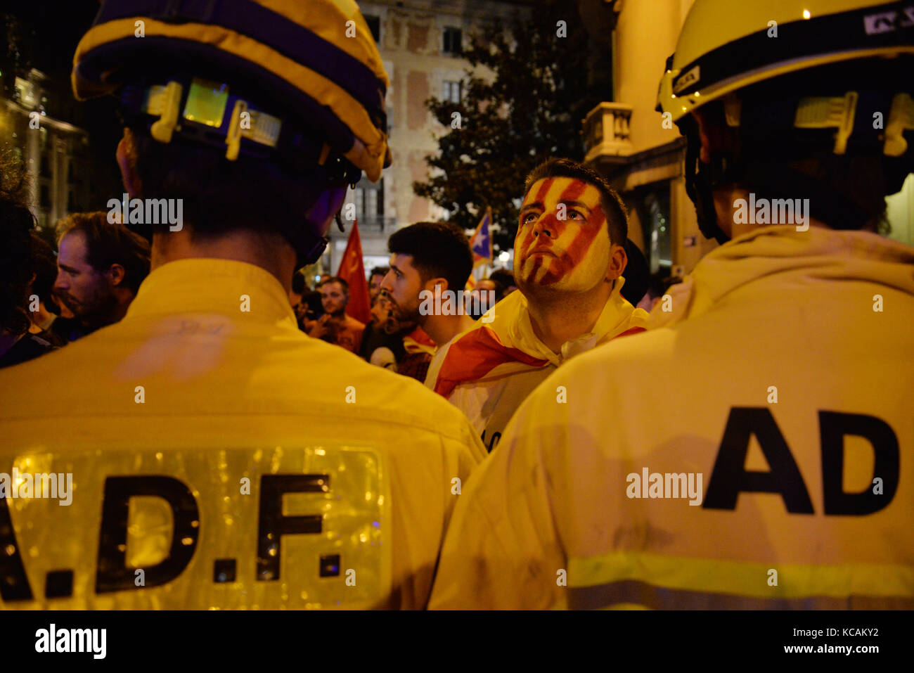 Barcelona, Spanien. 3. Oktober. Ein Mann mit der katalanischen Flagge auf seinem Gesicht gemalt aussieht, starrt auf die Policía Nacional, während Feuerwehrmänner Demonstranten zu überzeugen zu lassen Auseinandersetzungen in Barcelona während des Protestes gegen die spanische Regierung und das Verhalten der Polizei während der katalanischen Referendum zu vermeiden versuche, am 1. Oktober, während des Generalstreiks, die weit gefolgt wurde. Credit: laia Ros padulles/alamy leben Nachrichten Stockfoto