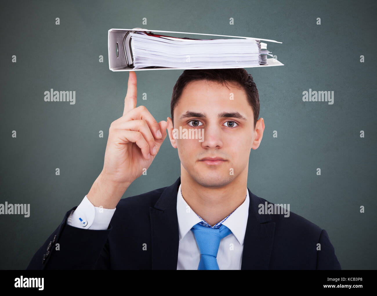 Portrait einer jungen Geschäftsmann Balancing Binder am Kopf auf grauem Hintergrund Stockfoto