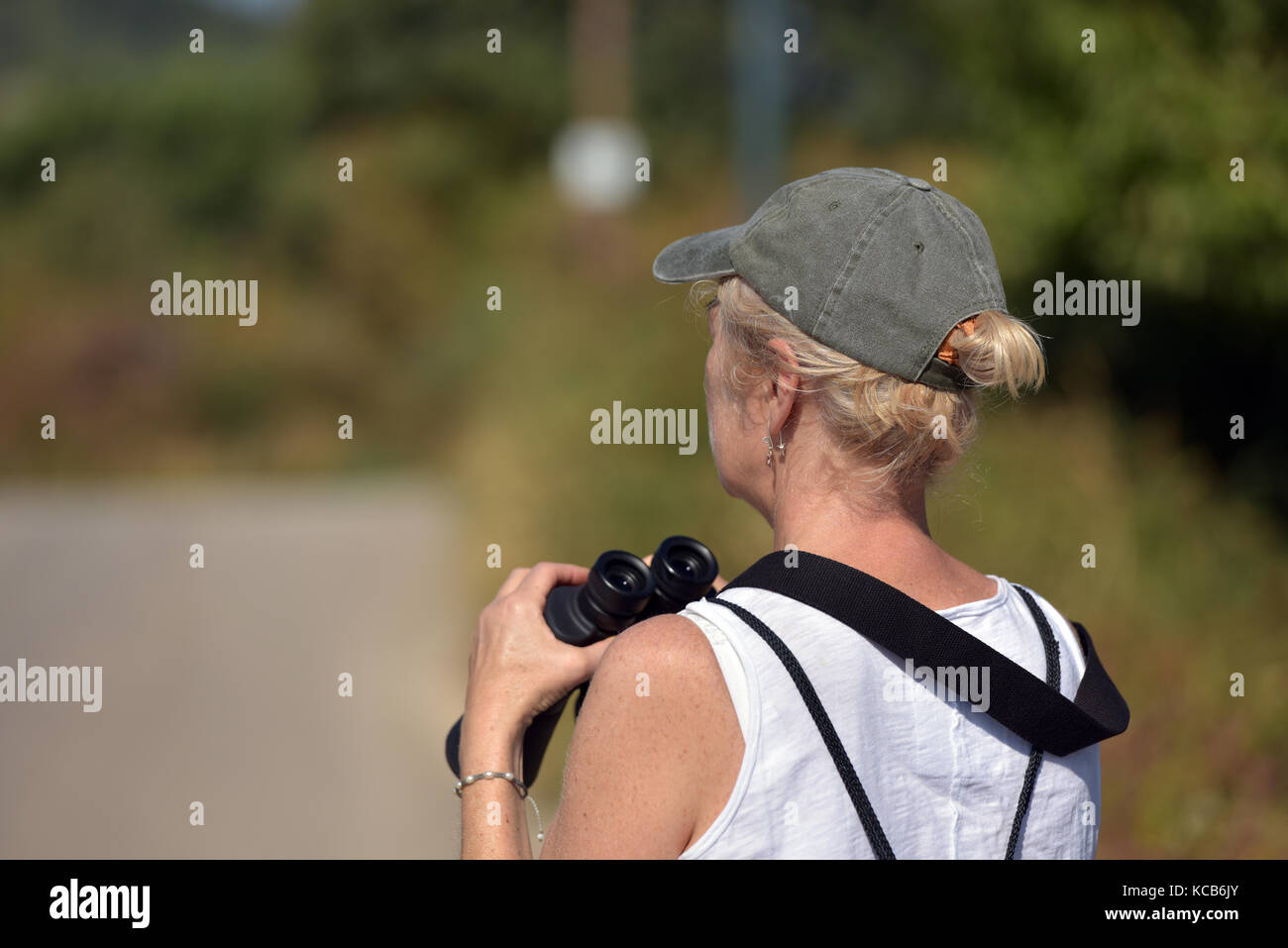Eine Frau trägt ein Baseball Cap und halten ein Fernglas birdwatching oder Vogelbeobachtung auf der Insel Korfu in Griechenland auf einen hellen und sonnigen Tag. Stockfoto