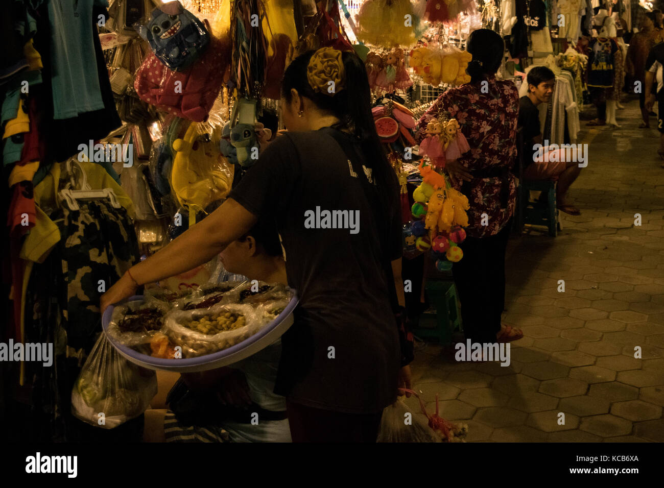 Asiatische Frau verkaufen Asiatische Fingerfood und behandelt in Phnom Penh Nacht Markt, mit einer Frau an ihrer Kleidung Stall, neben einem Spielzeug. Kambodscha Stockfoto
