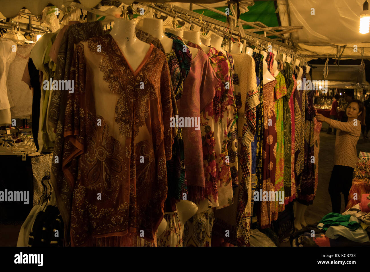 Eine Frau Anzeige und Verkauf kleider Night Market in Phnom Penh, Kambodscha, Süd Ost Asien. Bunte, günstige kleider mit wunderschönen ethnischen Mustern. Stockfoto