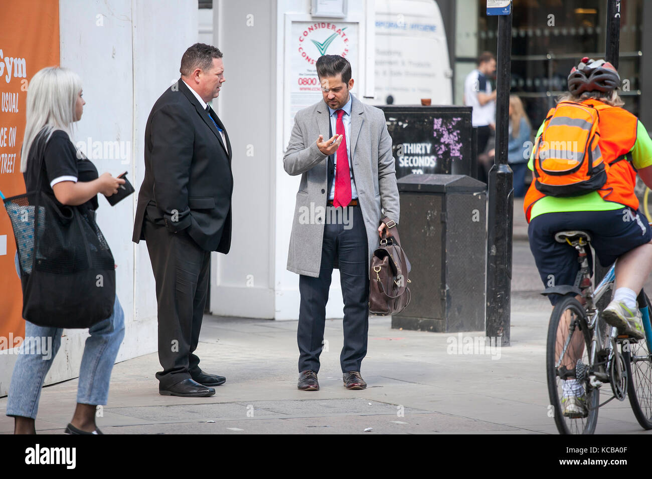 London, England - September 11, 2017 ein Mann in einem grauen Mantel im Telefon lesen und wartet auf seinen Freunden. Die Masse eilt durch Stockfoto