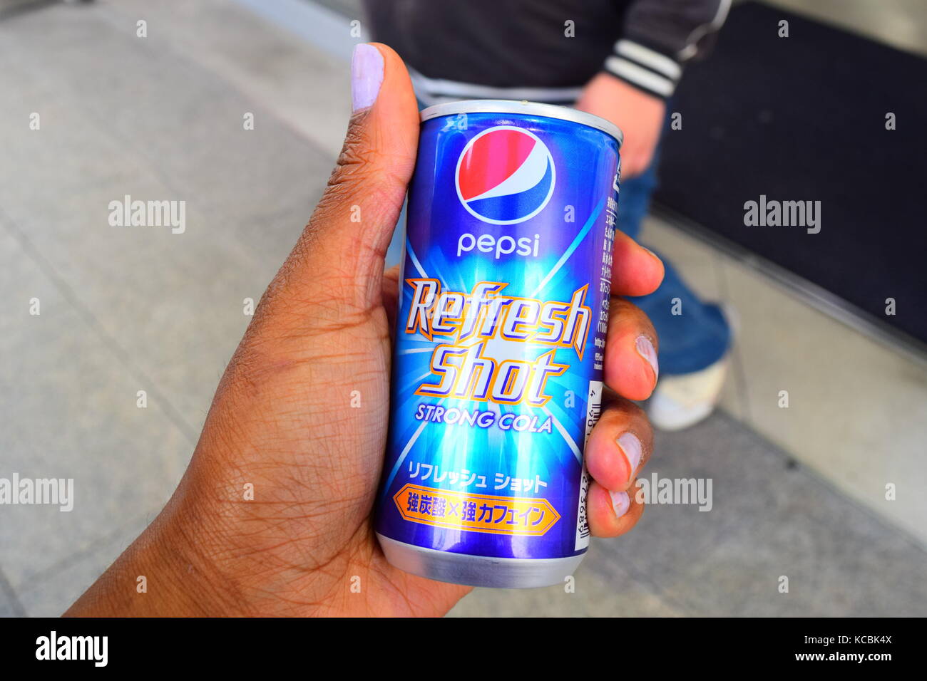 Schuß von der Hand des jungen Schwarz/Braun Frau mit einem kann der japanischen Pepsi Refresh Schuß starke Cola auf den Straßen von Japan mit Teenager im Hintergrund Stockfoto