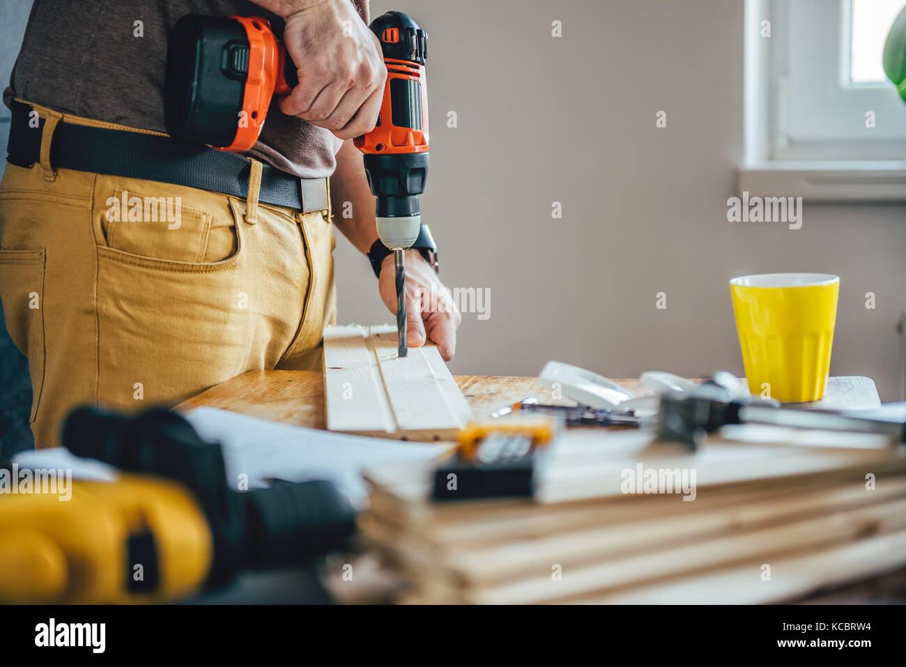 Man Bohren von Holz mit der Bohrmaschine auf dem Tisch zu Hause Stockfoto