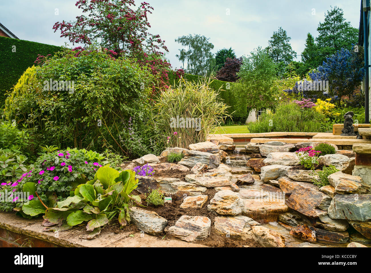 Eine neu gepflanzten Steingarten nach dem Installieren einer handgefertigten Naturstein Wasserfall in einem Englischen Garten in Großbritannien Stockfoto