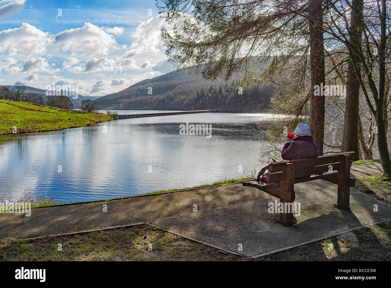 Landschaft mit einer Dame entspannen in der Kälte saß auf einer Bank mit Blick auf einen See oder Stausee Trinkwasser aus einem roten Schale Stockfoto