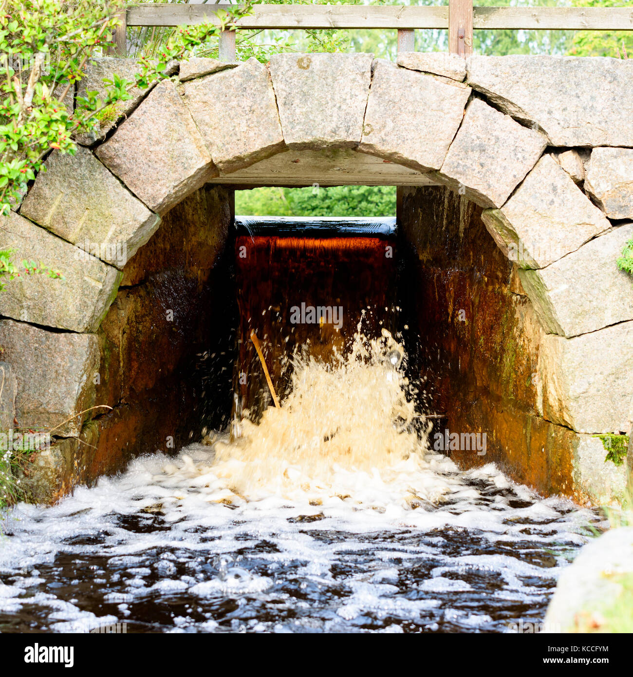 Kleiner Wasserfall von Überlauf unter einer Brücke aus Stein. Feines arch aus Granit Steinblöcken. Stockfoto