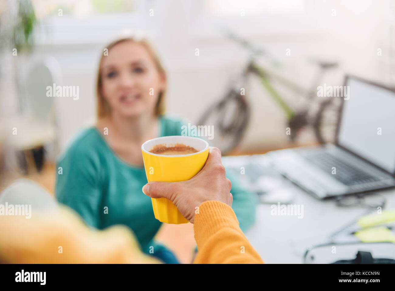 Frau mit gelben Kaffeetasse zu ihrer Kollegin im Büro Stockfoto