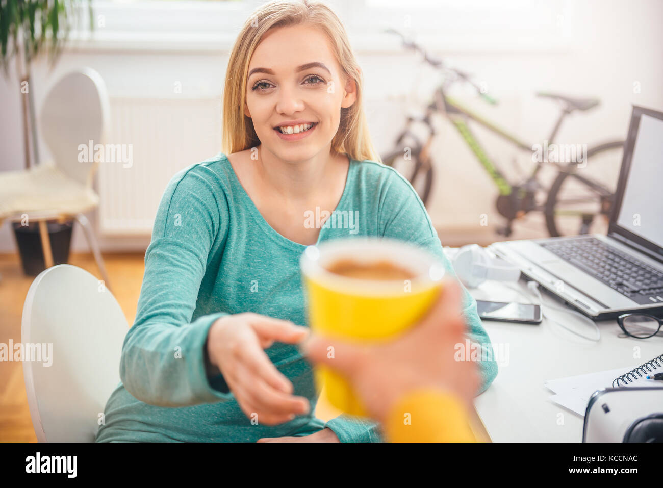 Frau mit gelben Kaffeetasse zu ihrer Kollegin im Büro Stockfoto
