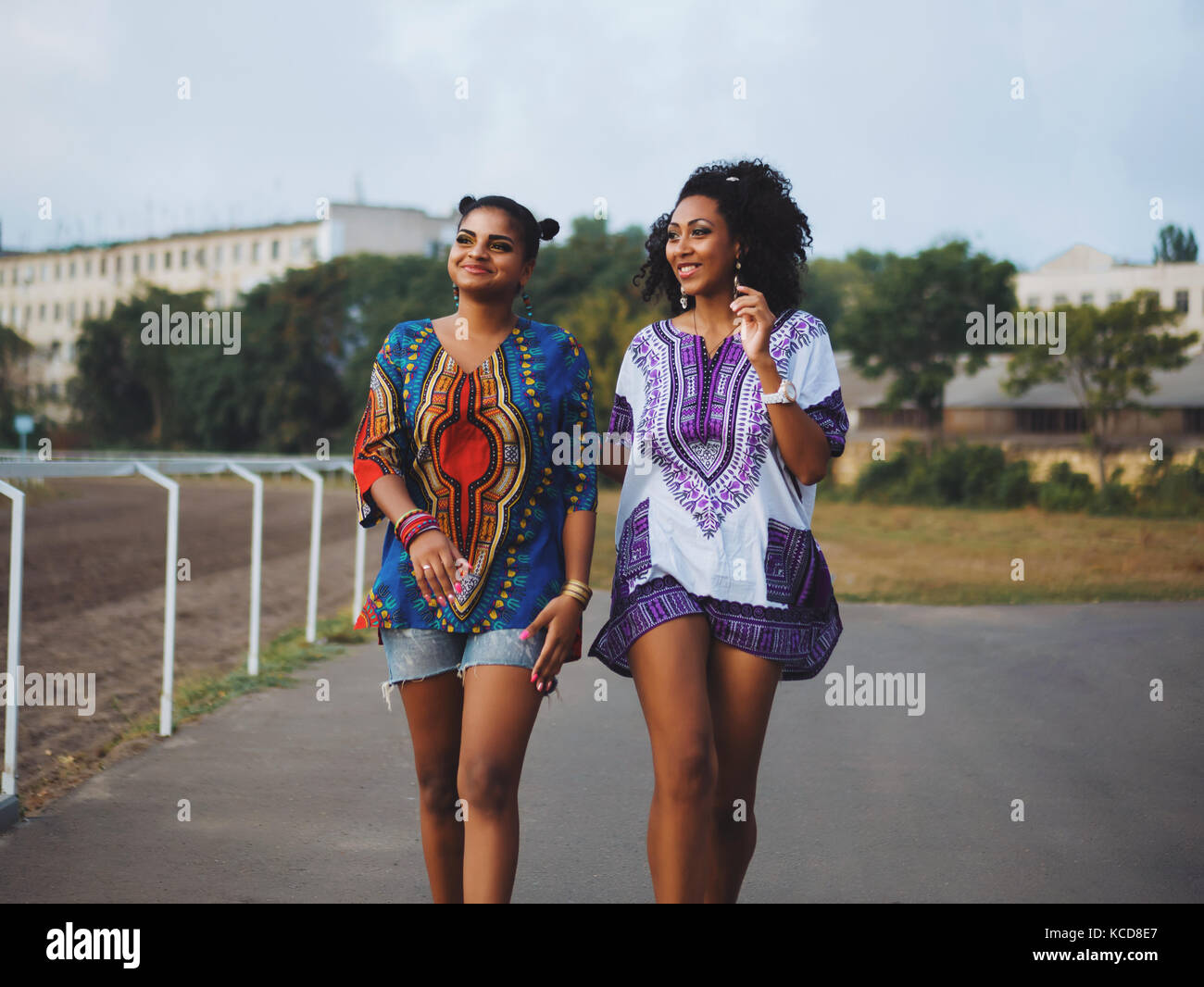 Zwei glückliche wunderschöne Afro-amerikanische Frauen, die Freunde wandern Outdoor. Jungen gemischten Rennen Mädchen tragen bunte Kleidung kommuniziert, genießt die Sitzung und Lachen Stockfoto