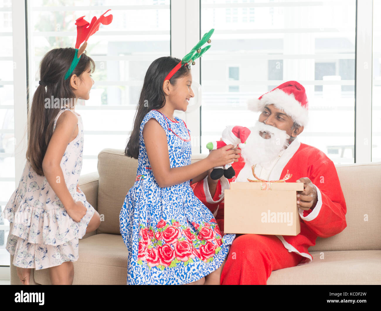 Gerne indische Familie feiern Weihnachten Urlaub, mit Geschenkbox und Santa auf der Couch zu Hause sitzen, asiatischen Menschen festival Stimmung drinnen. Stockfoto