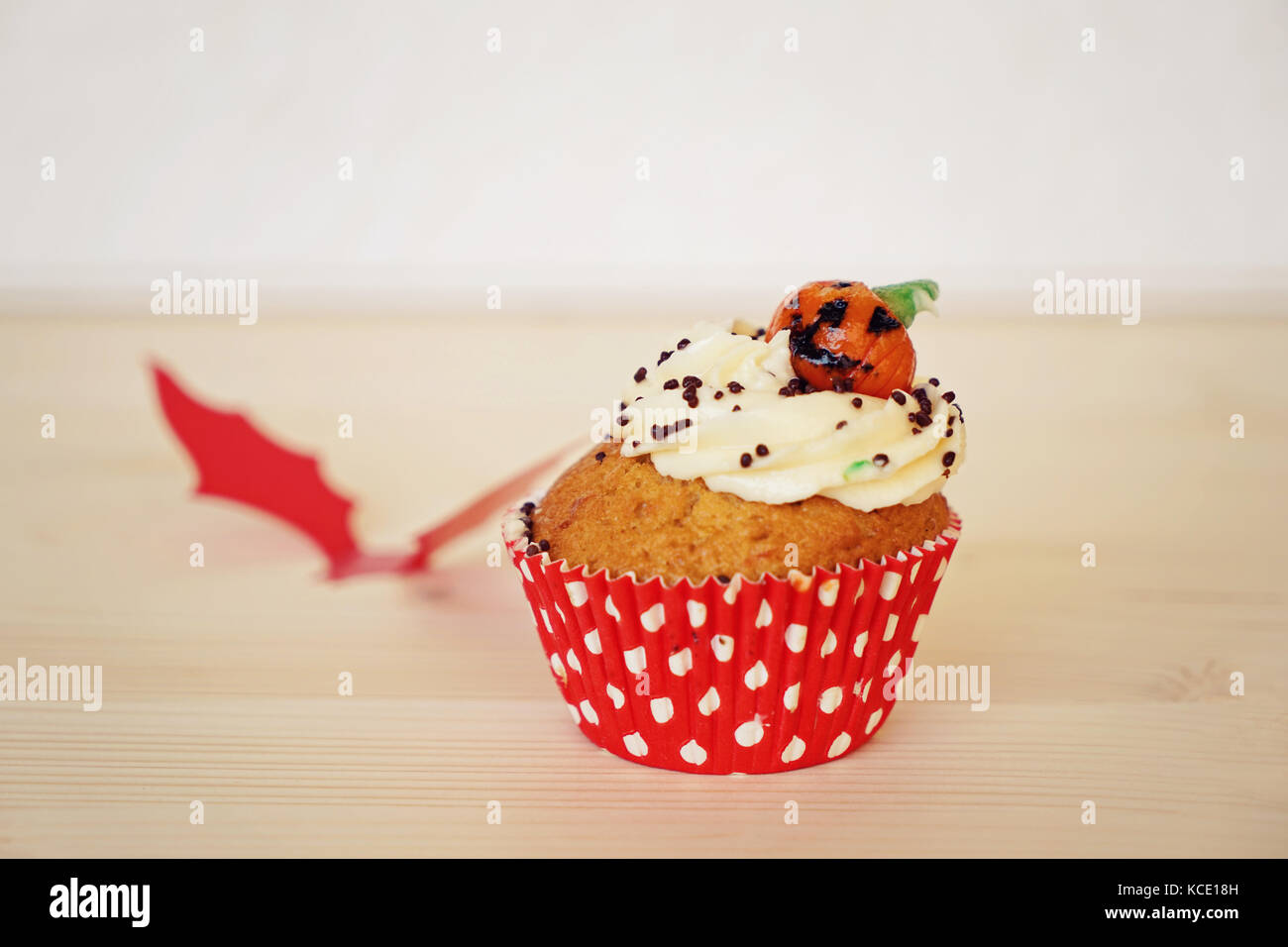 Cupcake mit Sahne und Marzipan Kürbis an Halloween auf dem beigen Hintergrund und roten bat eingerichtet Stockfoto