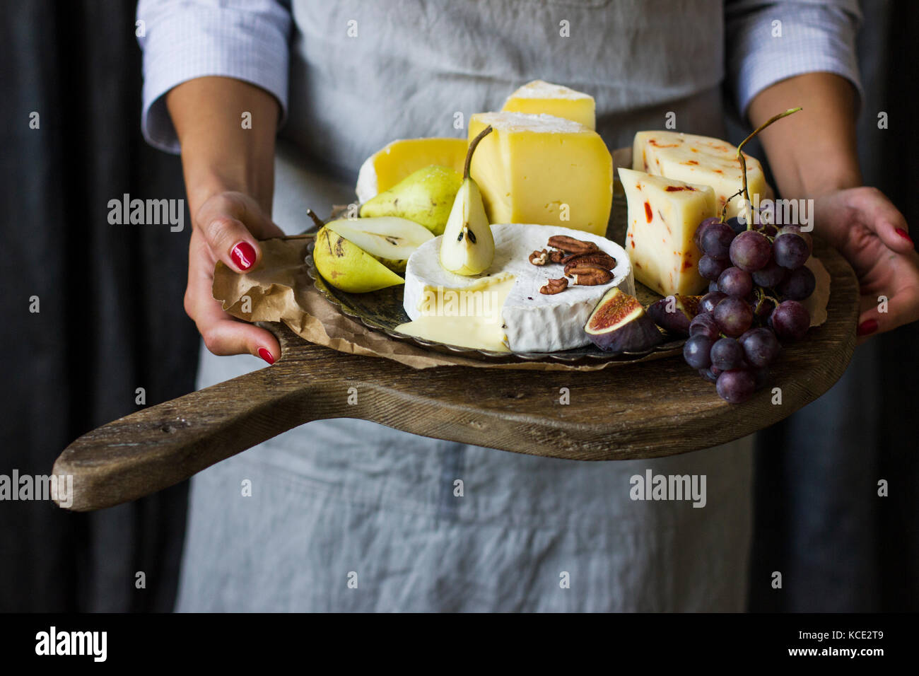 Junge Frau mit einer Platte mit Käse auf dem Holzbrett Stockfoto