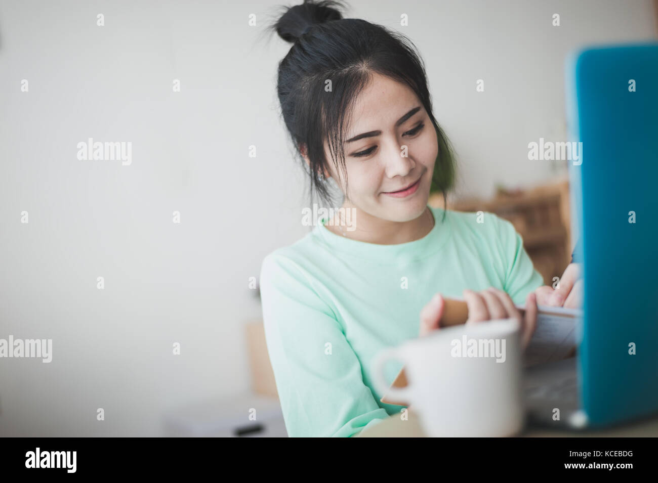 Junge attraktive Asiatin freelancer Schreiben auf Notebook, indem Sie mit der linken Hand während der Arbeit mit dem Laptop. die Arbeit zu Hause und online learning Konzept Stockfoto