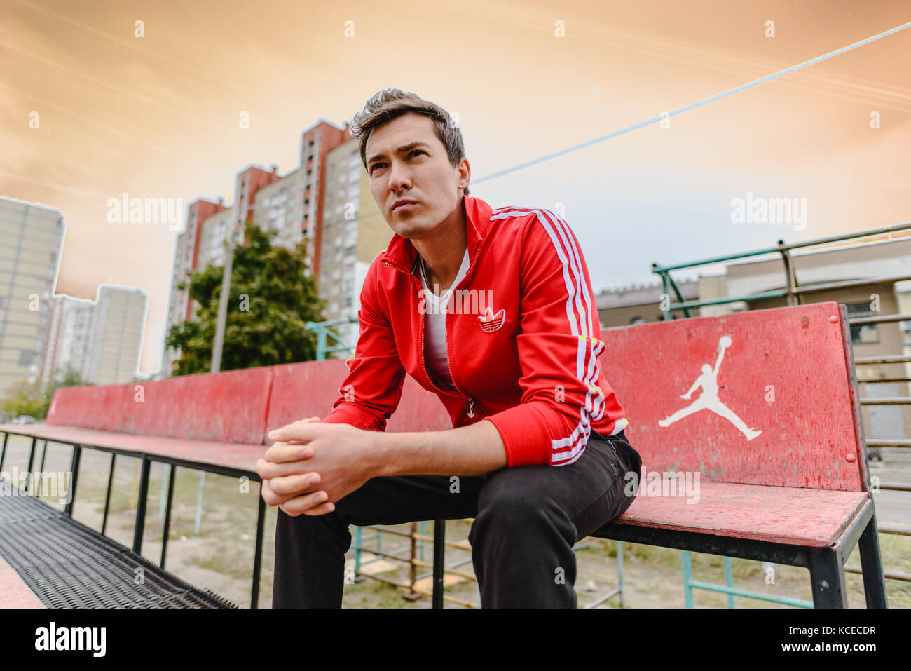 Junger Mann in einem roten Sport Anzug sitzt auf einem Sport Stockfoto
