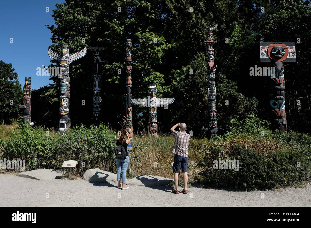 Zwei Touristen bewundern die neun Totem Pole auf der Kaimauer des Stanley Parks in Vancouver, British Columbia, Kanada. Stockfoto