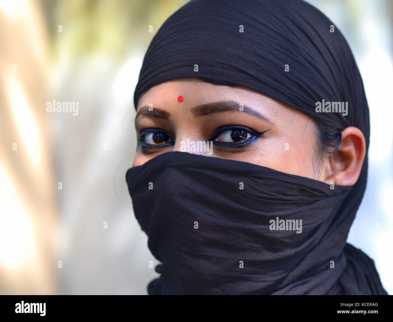 Dreiviertel Blick auf eine junge Assamesische hinduistische Schönheit mit mandelförmigen Augen, die ihr Haar und Gesicht mit einem säkularen, trendigen schwarzen Kopftuch bedeckt Stockfoto