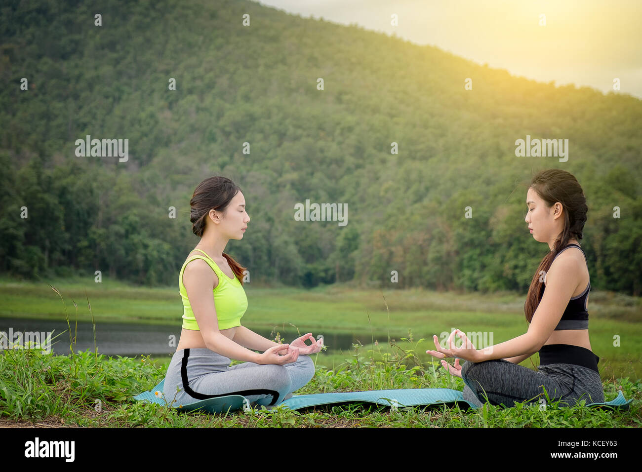 Zwei junge womans sitzen Yoga in der Nähe des Flusses. Konzept der gesunden Lebensstil und Entspannung. Stockfoto