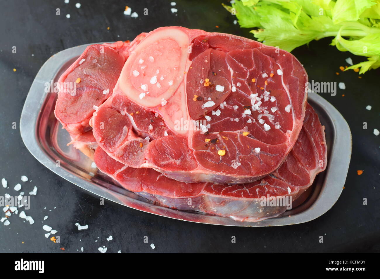 Rohes Rindfleisch Fleisch mit Knochen. ossobuco Fleisch auf einem Metallauflagefach auf einem grauen Abstrakt Hintergrund mit einigen grünen frischen Sellerie verlässt. traditionellen italienischen Essen Stockfoto