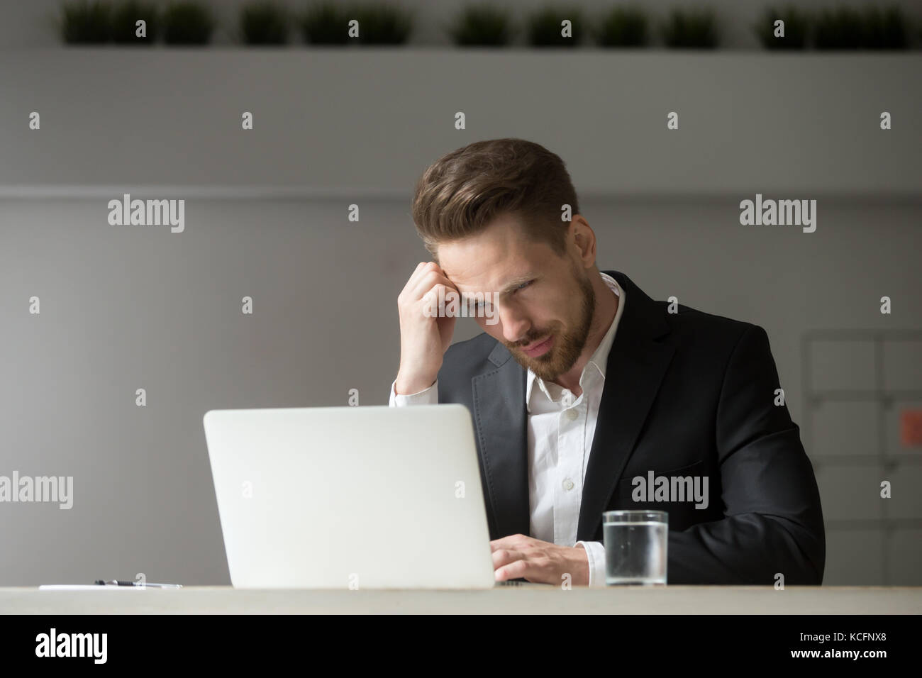Ratlos und verwirrt gut aussehender Geschäftsmann am Laptop Bildschirm am Arbeitsplatz im Büro suchen. Junge Geschäftsführer oder Projektleiter ist nicht sicher, ob er Ag sollte Stockfoto