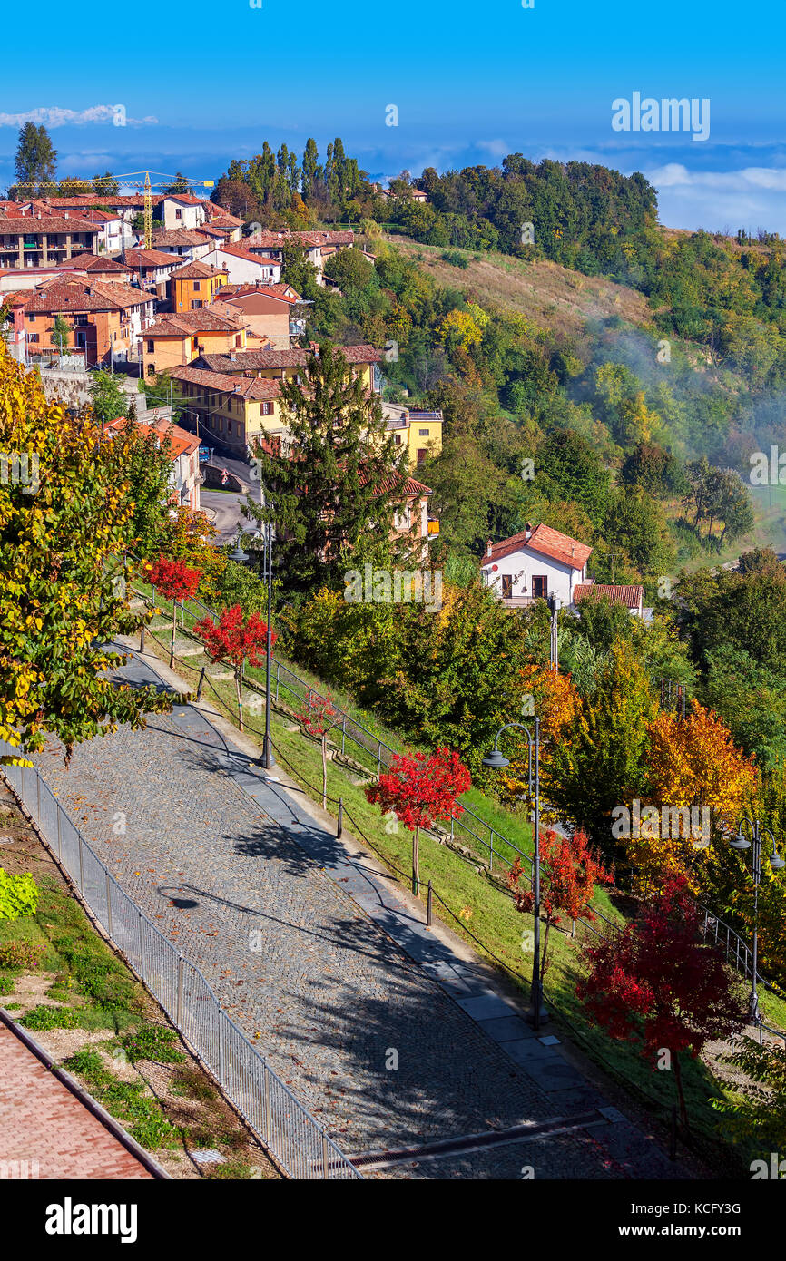 Blick von oben auf die Gasse entlang Bunte herbstliche Bäume und Hügel, die als kleines Dorf auf Hintergrund in Piemont, Norditalien (vertikale Komposition). Stockfoto