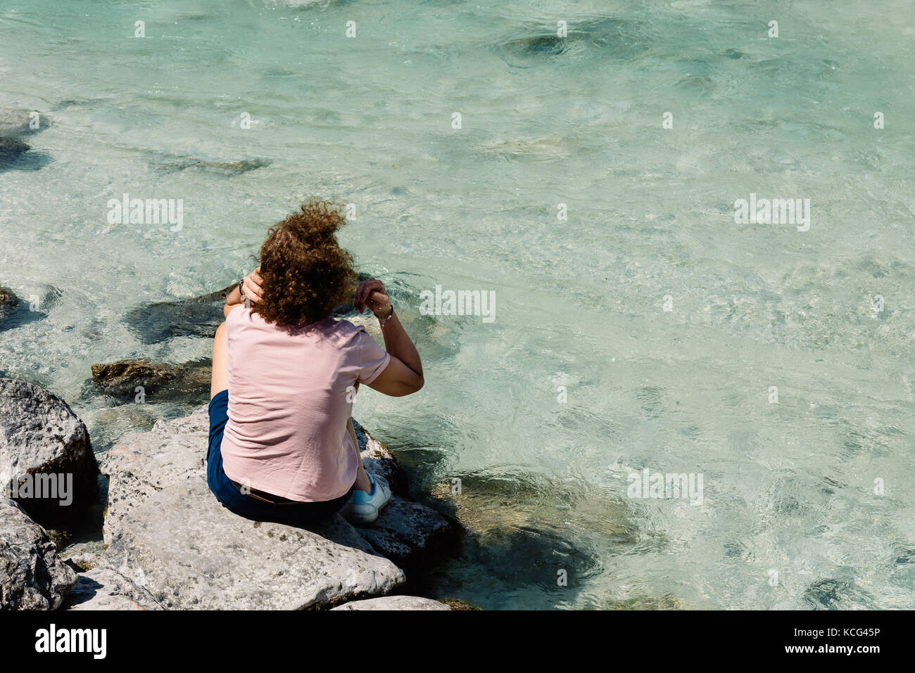 Frau sitzt auf einem Felsen durch einen Wasserstrahl in die Berge Stockfoto