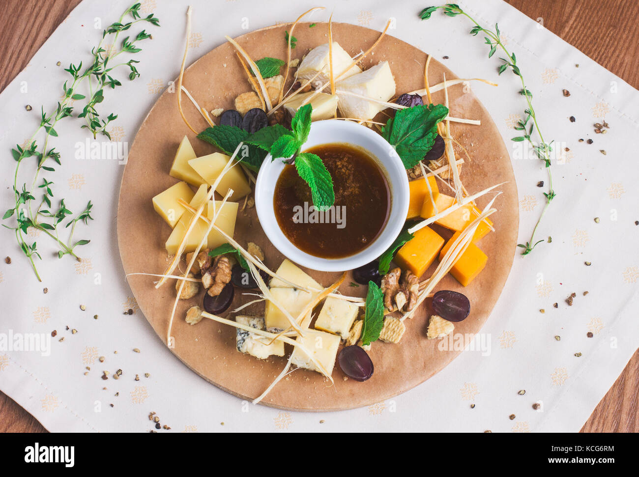 Verschiedene Arten von Käse mit Honig, Nüssen und Früchten auf runden Holzbrett Stockfoto