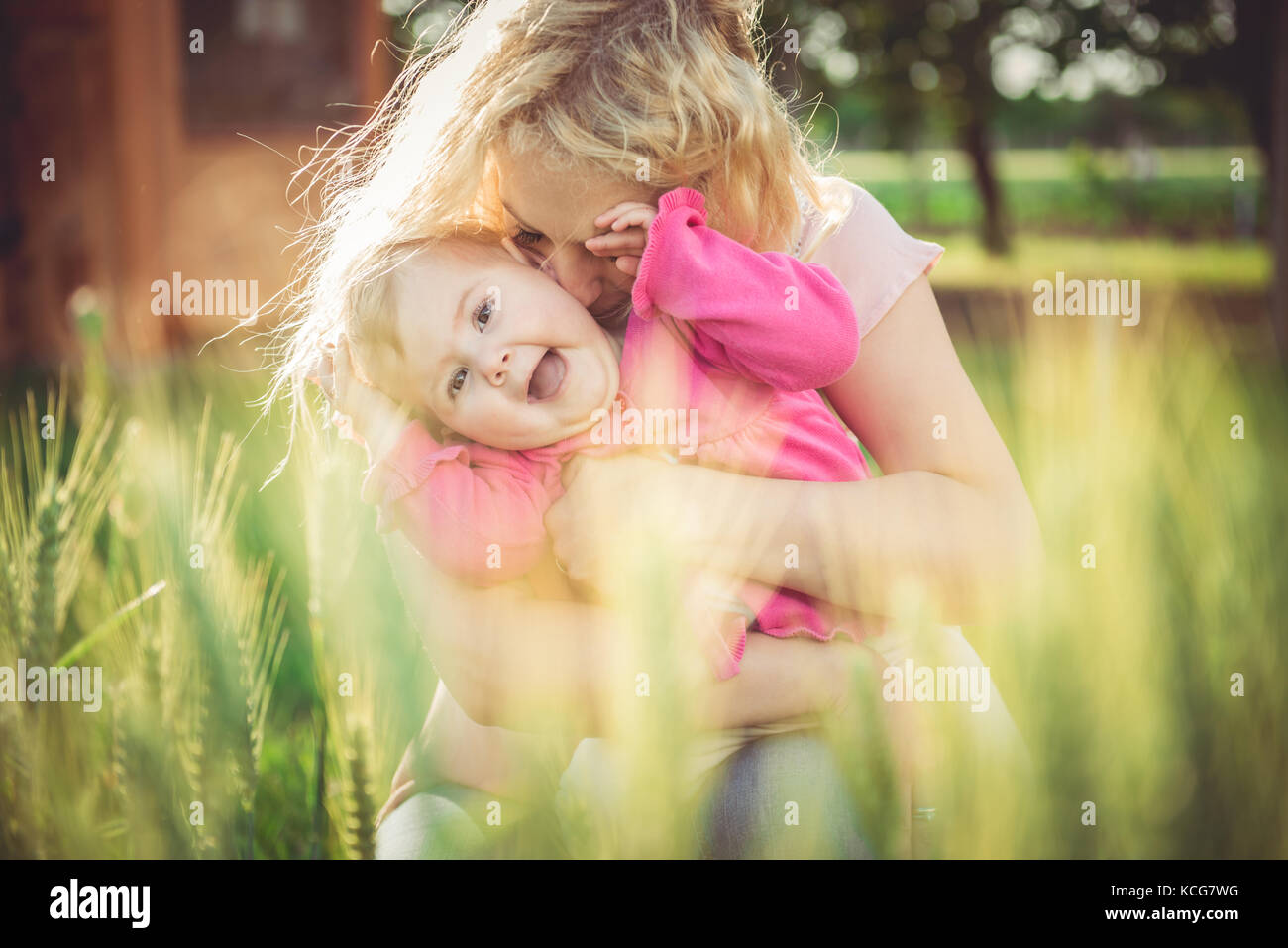 Junge Mutter halten und küssen ihr Baby im Gras Stockfoto