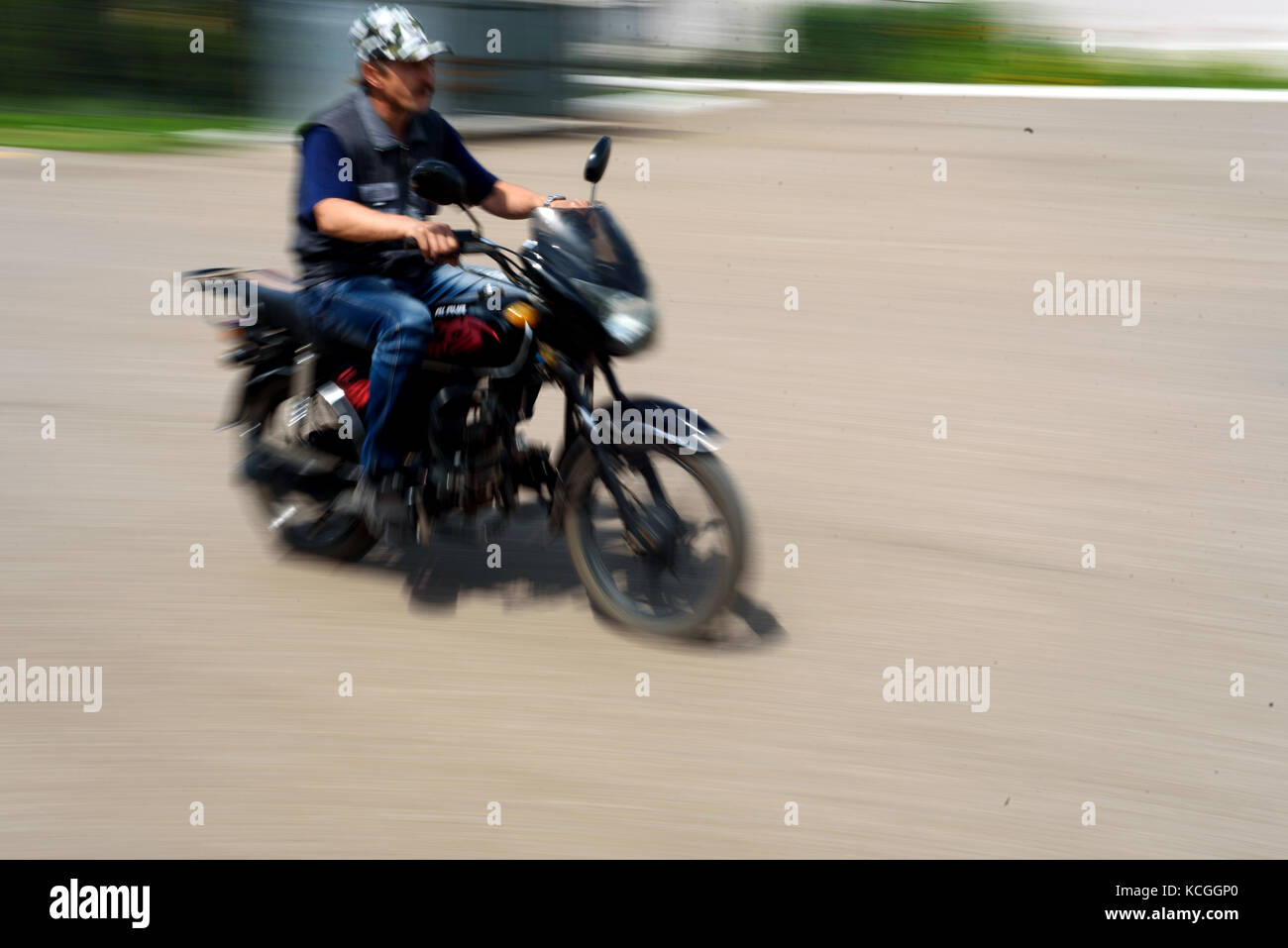 Mann ohne Helm reitet sein Motorrad mit absichtlichen Bewegungsunschärfe der Bewegung des Reiters und die fahrräder Geschwindigkeit Stockfoto