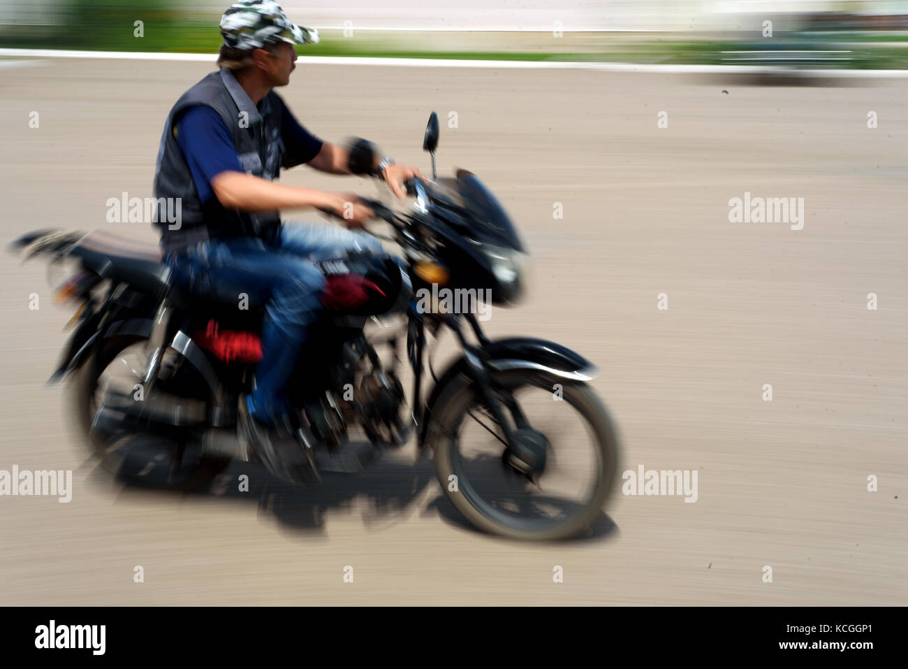 Mann ohne Helm reitet sein Motorrad mit absichtlichen Bewegungsunschärfe der Bewegung des Reiters und die fahrräder Geschwindigkeit Stockfoto