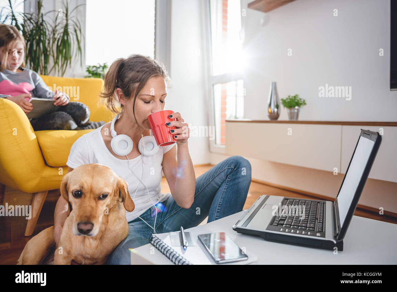 Frau mit weißem T-Shirt sitzen auf dem Boden in der Tabelle Kaffee trinken und einen Streichelzoo, einen Hund Stockfoto
