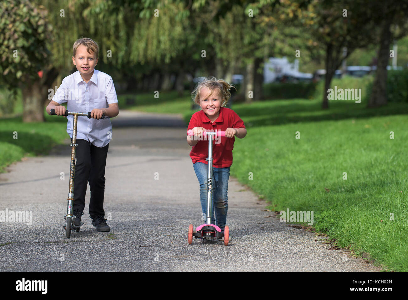 Kinder reiten ihre Roller - ein kleiner Junge und seine kleine Schwester, die Spaß Rennen entlang eines Weges auf ihren Motorroller. Stockfoto