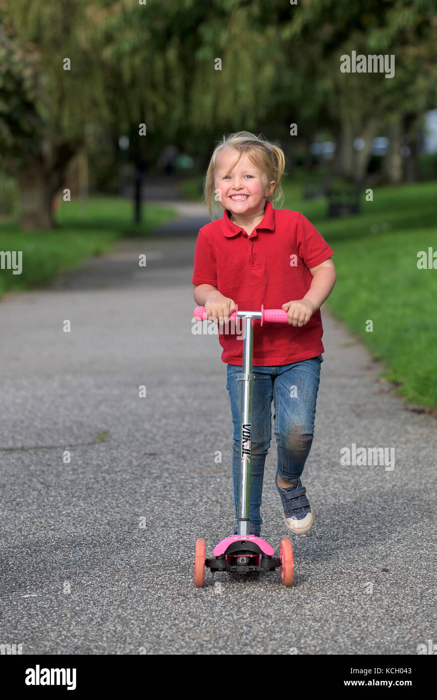 Ein Kind, das einen Roller reitet - ein junges Mädchen, das Spaß hat, ihren Roller entlang eines Pfades zu reiten. Stockfoto
