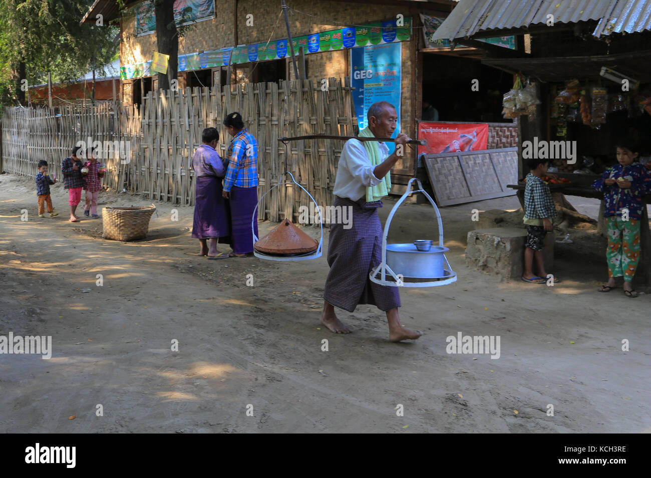 Ein Mann im Dorf Yandabo auf dem Irrawaddy Fluss in Myanmar (Birma) ist die Töpfe mit Essen, während Frauen und Kinder in der Nähe von einem Geschäft stehen. Stockfoto