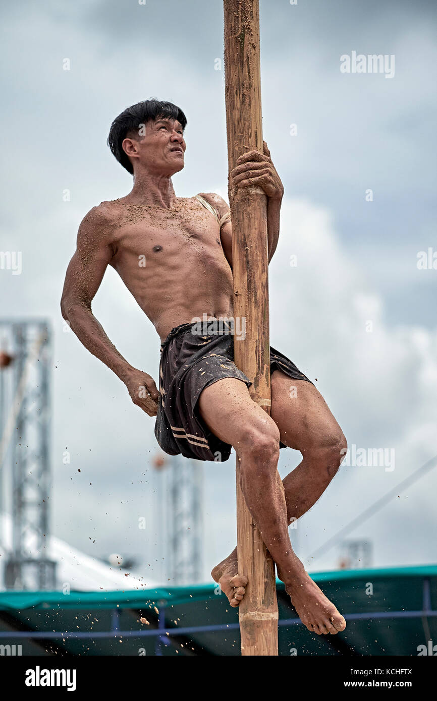 Thailand Mann zeigen, wie eine nasse slippy Pole mit Hilfe von Sand zu klettern als Greifer. Stockfoto