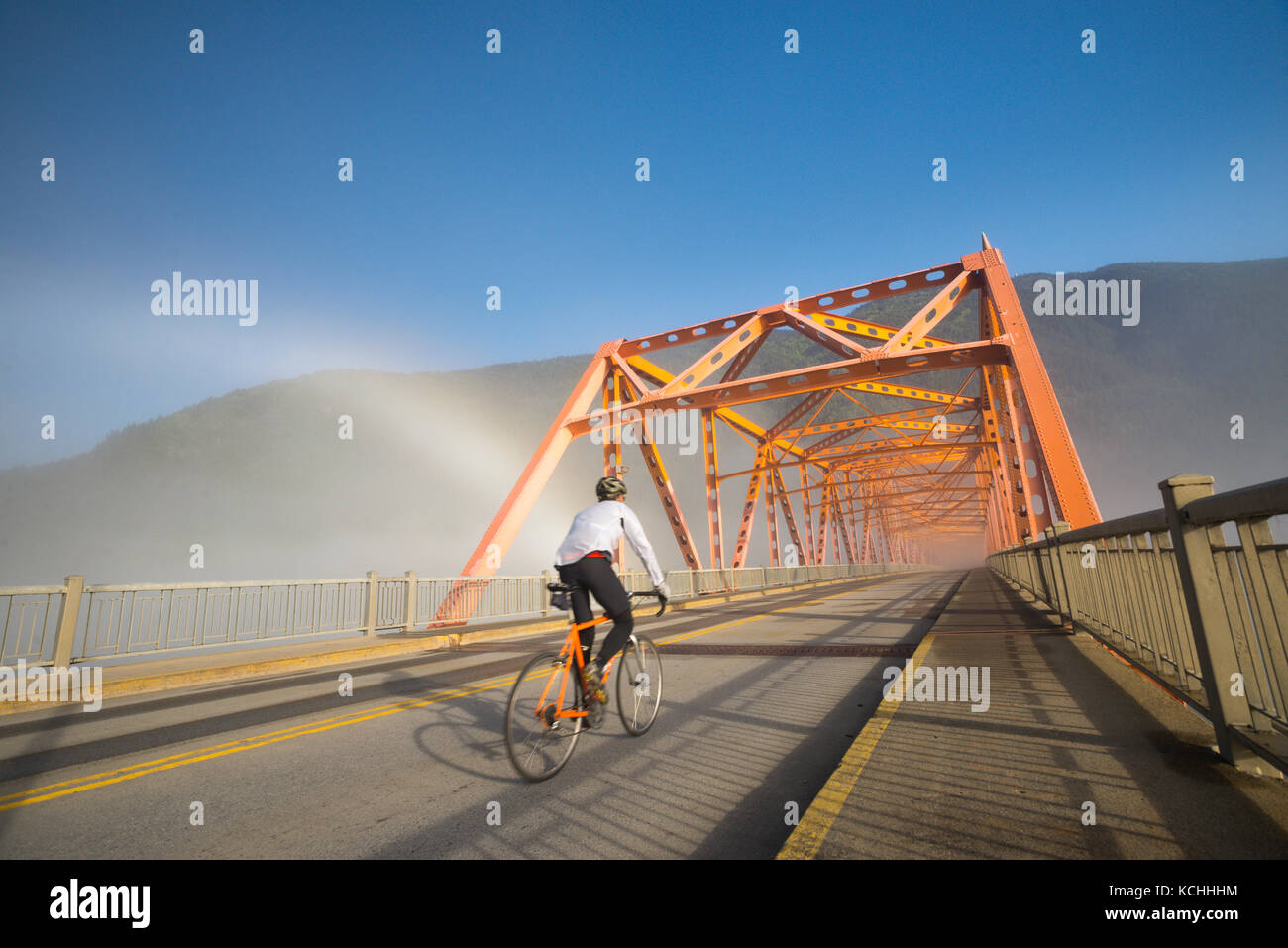 Ein Mann fährt mit dem Rennrad auf den Weg, während eine brockenspecter hinter ihm in Nelson, BC leuchtet Stockfoto