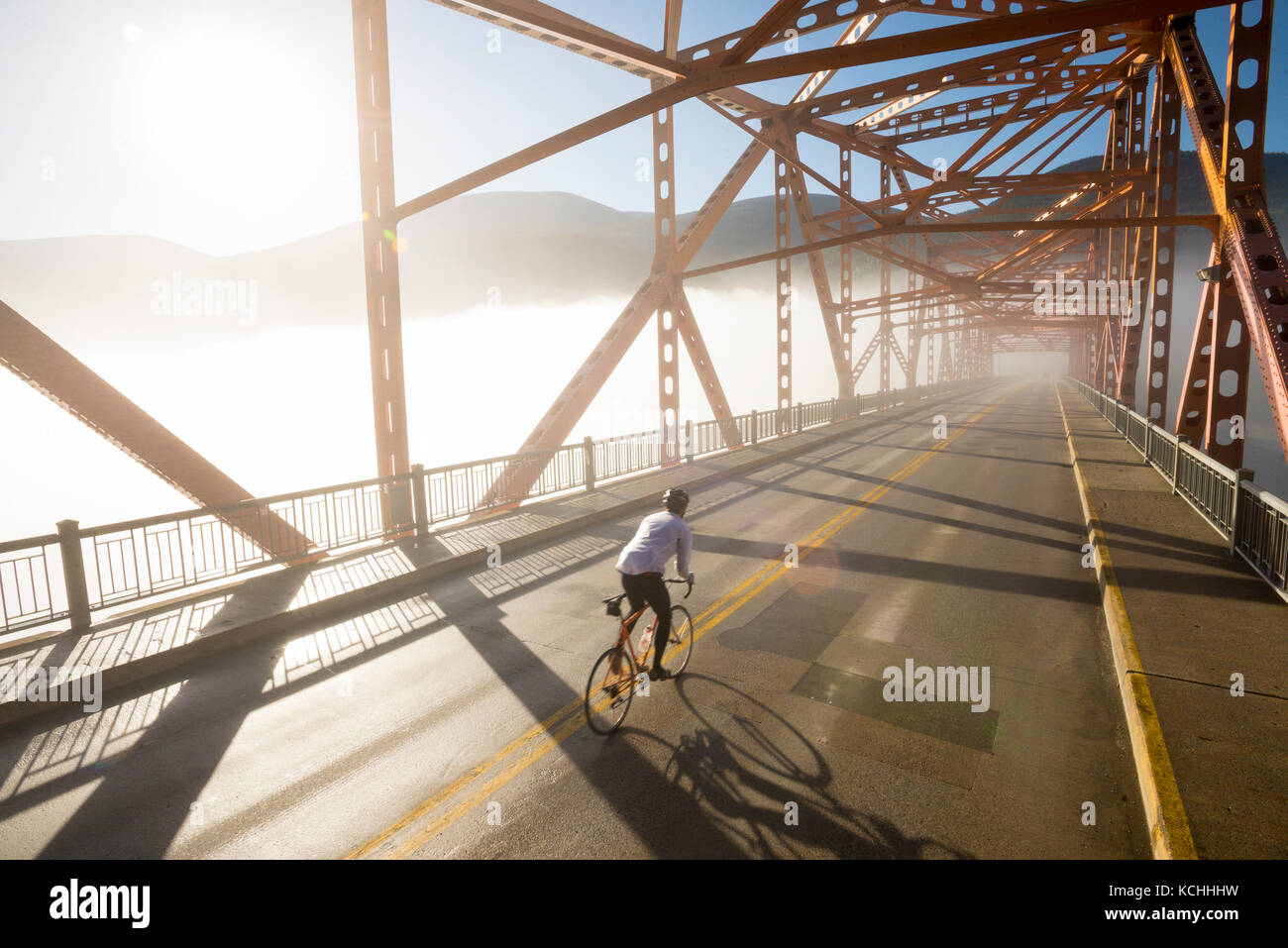 Ein Mann fährt mit dem Rennrad auf einem großen orange Brücke während der morgendlichen Fahrt zum Arbeitsplatz in Nelson, BC Stockfoto