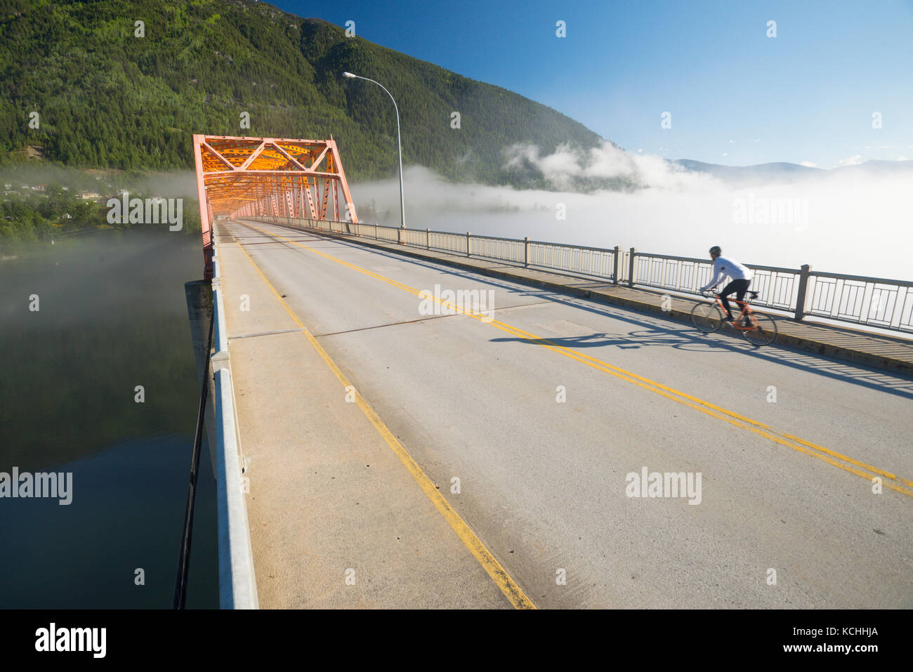 Ein Mann fährt mit dem Rennrad auf den Weg über die grosse orange Brücke in Nelson, BC Stockfoto