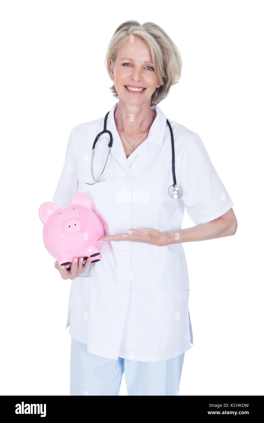 Reife Frau Doktor Holding Sparschwein Over White Background Stockfoto Reife Frau Doktor Holding Sparschwein Over White Background Stockfoto