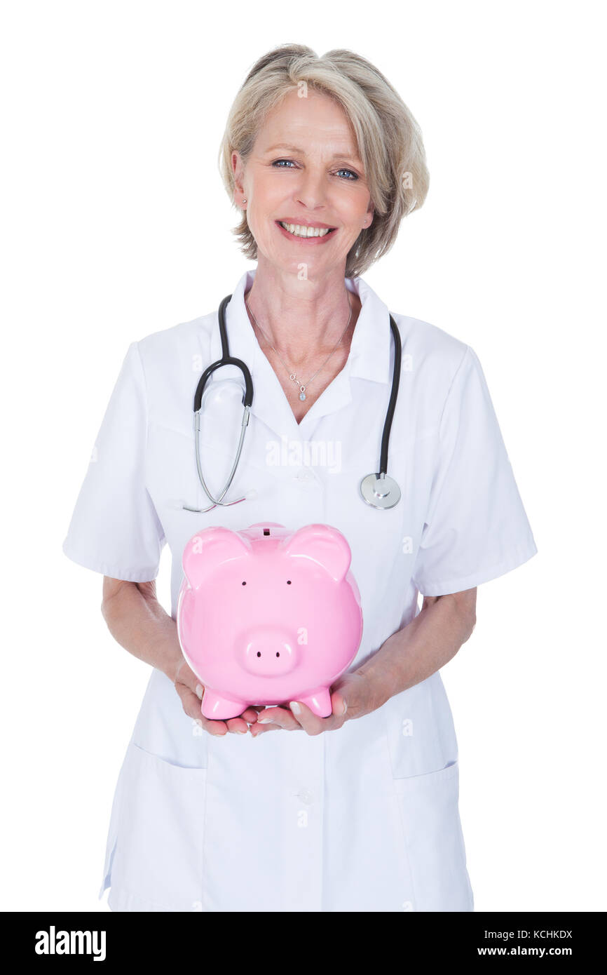 Reife Frau Doktor Holding Sparschwein Over White Background Stockfoto Reife Frau Doktor Holding Sparschwein Over White Background Stockfoto