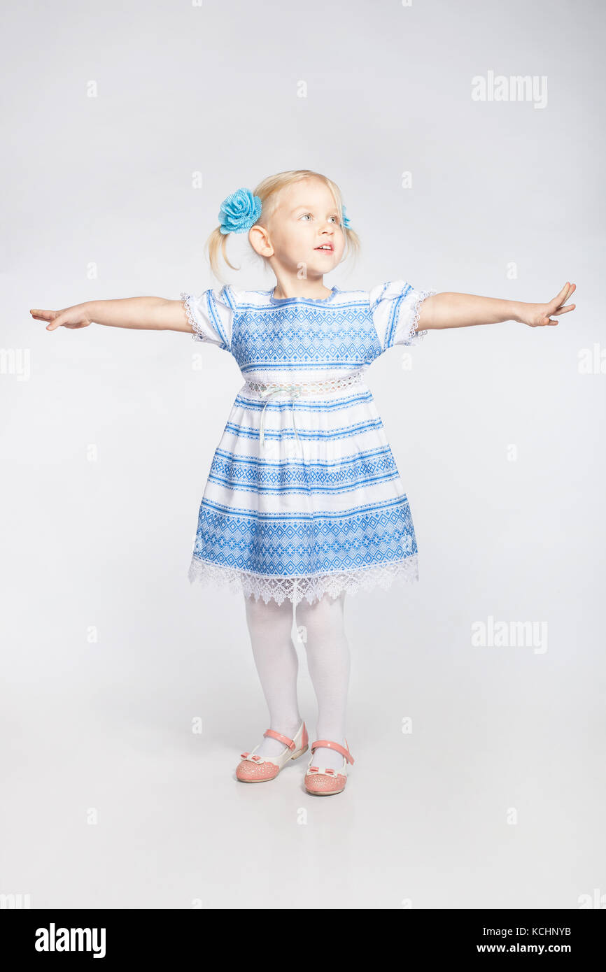 Kleine blonde Mädchen stehen mit ausgestreckten Armen auf einem weißen Hintergrund Stockfoto